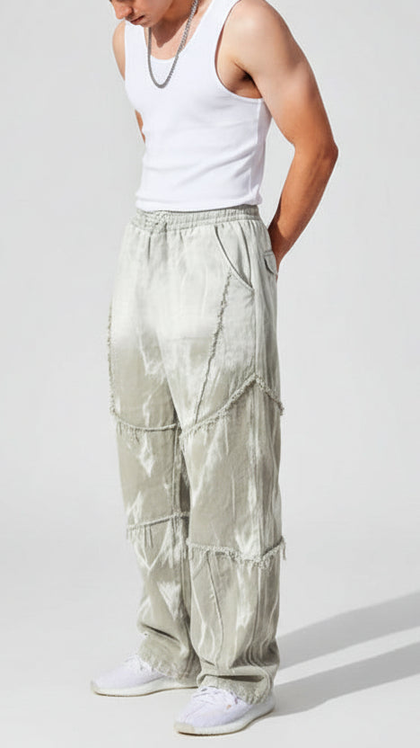 Person wearing a white tank top and light-colored pants leaning against a beige stone wall.